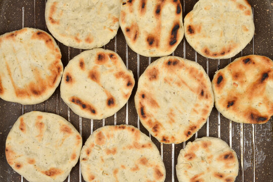 A close-up, top-down view shows several round flatbreads with golden-brown marks being cooked directly on the dark ribbed surface of a grill pan
