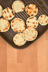 Several round flatbreads are on a ribbed, dark non-stick pan, showing distinct golden-brown grill marks on a wooden surface