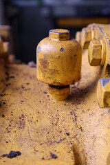 Close-up of a large, oil-stained or oil breather, yellow cover bolt and industrial housing surface, showing heavy-duty mechanics, grit, and wear in a maintenance environment.