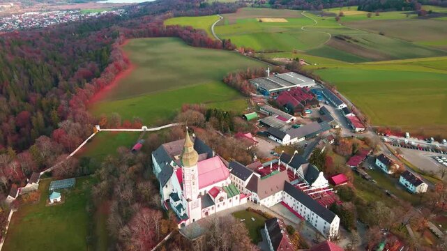 Aerial view of the magnificent Andechs Abbey with its red roofs and golden dome, surrounded by autumn colored trees and green fields, Andechs, Bayern, Germany.