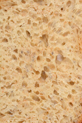 An extreme close-up, full-frame background of the porous, airy crumb texture of a slice of light-colored artisan bread with visible seeds