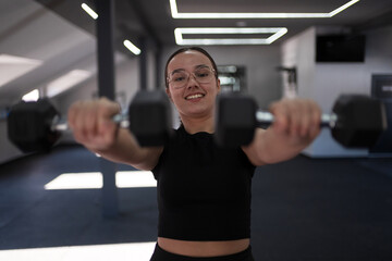 Smiling woman lifting dumbbells in a bright gym setting during the day