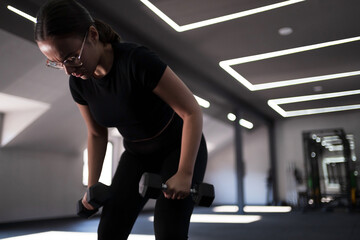 Young woman exercises with dumbbells in a modern gym during a fitness session in the afternoon