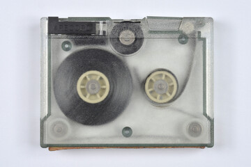 An overhead shot of a vintage gray data cartridge or tape cassette with a clear plastic top, revealing the inner reels and tape mechanism