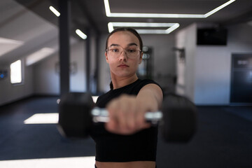Young woman lifting dumbbell in modern fitness center during a workout session focusing on strength training and exercise