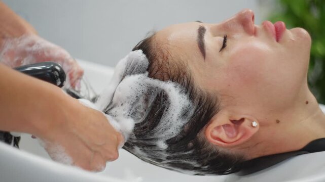 The hairdresser applies shampoo to the client's head, lathers it up, and massages it. High quality 4k footage