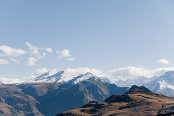 Snow-capped mountains in Kabardino-Balkaria under a cloudy sky. The landscape features rugged peaks and valleys, showcasing the natural beauty of the region.