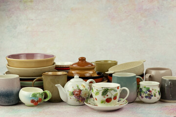 A variety of dishes on a textured background. Ceramic and plastic plates and mugs on the table. Houseware in the form of dishes.