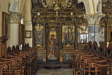 richly decorated iconostasis with gold accents and religious paintings, including icons of saints and biblical scene, arched architectural details in The Panagia Tourliani monastery in Mykonos 