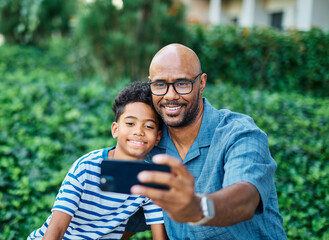 Portrait of father and son having fun using a mobile phone and taking a selfie photo with camera outdoors in park or nature,, family life, parenting, love and bonding concepts