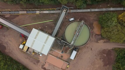 Aerial view of an industrial site with a large round tank and conveyor belts surrounded by red earth and green trees, Sileby, England, United Kingdom.