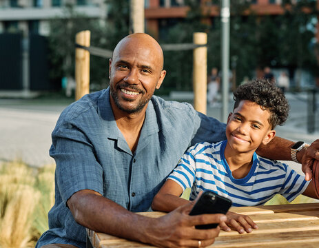 Portrait of father and son having fun using a mobile phone outdoors in park or nature,, family life, parenting, love and bonding concepts
