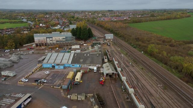 Aerial view of train tracks cutting through the landscape, industrial buildings, and scattered cars, with muted autumnal colors, Sileby, England, United Kingdom.