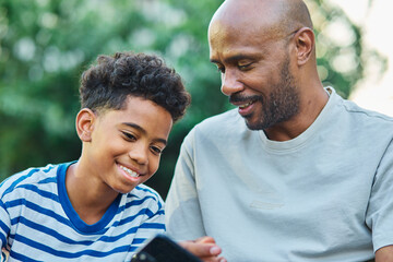 Portrait of father and son having fun using a mobile phone outdoors in park or nature,, family...