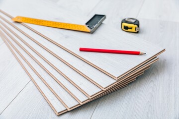 Wooden laminate flooring planks and measuring tools for a home improvement project on a light colored floor surface