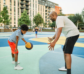 African american father and boy smiling, standing together playing basketball on a colorful...