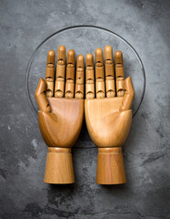 A pair of rustic, simple wooden hands are clasped together in the center of a large, empty stone surface.