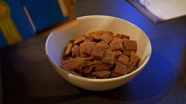 Filling white bowl with shreddies wheat cereal for breakfast