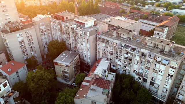 Aerial drone view of Belgrade Serbia brutalist residential buildings at sunset, showing raw concrete architecture, warm evening light, and dense urban landscape