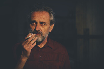 Fototapeta premium Older man in red shirt waiting for something and smoking on night city location