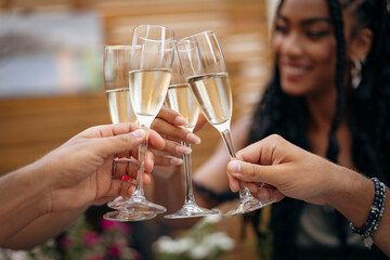 Diverse friends making a cheers with champagne at a celebration party. Close up of hands clinking...