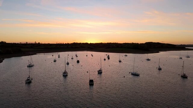 Aerial view of boats at dusk, floating peacefully on the tranquil waters of Rutland Water under a sky painted with warm hues, Oakham, England, United Kingdom.