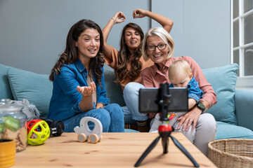 Three generations share a joyful video call—two women and their mother laugh while a baby plays...