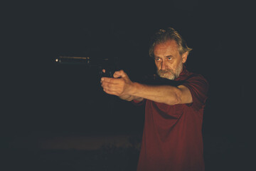 Older man in red shirt manipulating with handgun on night city location