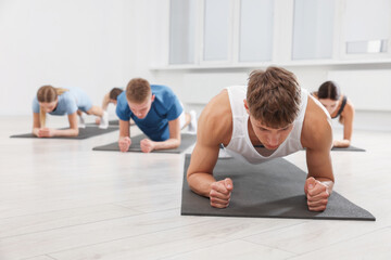Group of people doing plank exercise on fitness mats in gym, selective focus