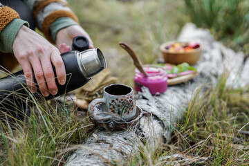 Healthy breakfast in the nature, eating home made bread and beet root pesto, drinking natural herbal tea