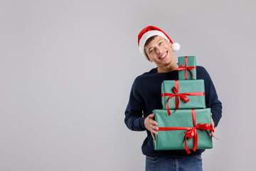 Smiling man in Santa hat with many gift boxes on grey background, space for text. Christmas and New Year celebration