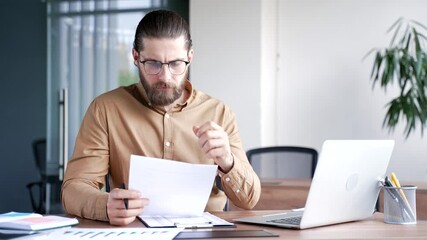 Busy thoughtful businessman analyzing financial documents checking data on laptop while sitting at a workplace in a business office. Financier deals with financial report, thinks over working details - Powered by Adobe