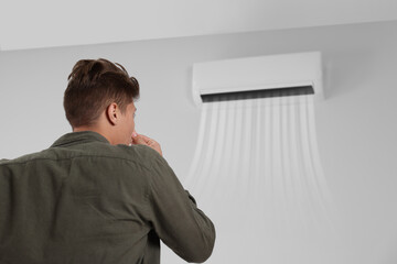Fototapeta premium Young man suffering from bad smell from air conditioner and covering his nose indoors