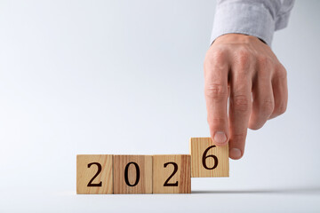 New 2026 year. Man putting cube with number 6 on light grey background, closeup
