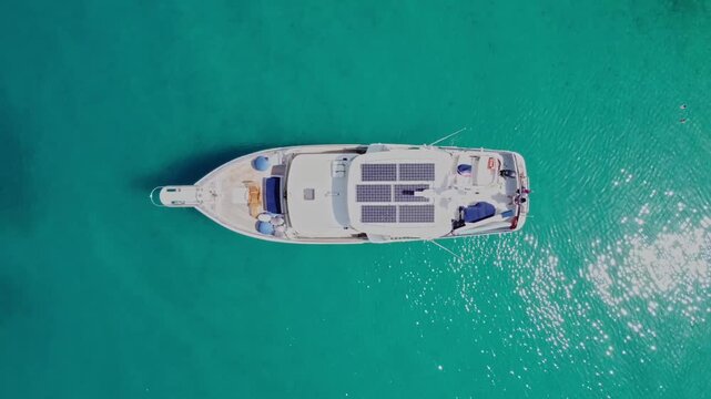 Drone overhead footage of a solar-powered boat gliding across bright blue sea on a sunny day, showcasing renewable energy technology and serene ocean scenery.