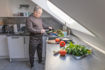 A man is preparing a fresh vegetables salad in the kitchen. Healthy food cooking.