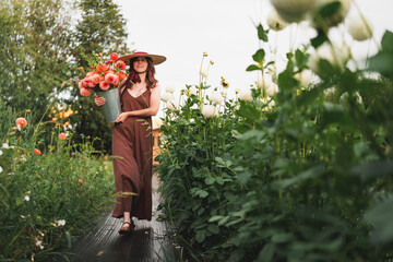 Woman with cheerful expression walking in a flower garden holding a bucket of dahlias