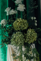 Elegant floral arrangement with green hydrangeas and white roses on table with green backdrop