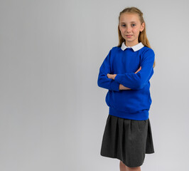 Confident schoolgirl standing with folded arms in blue pullover and grey skirt. Classic children’s school uniform showcasing cozy knit texture, smart classroom style, and autumn academic fashion
