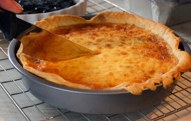 Close-up View of a Hand Slicing a Golden Brown Savory Quiche or Tart in a Round Baking Tin on a Cooling Rack