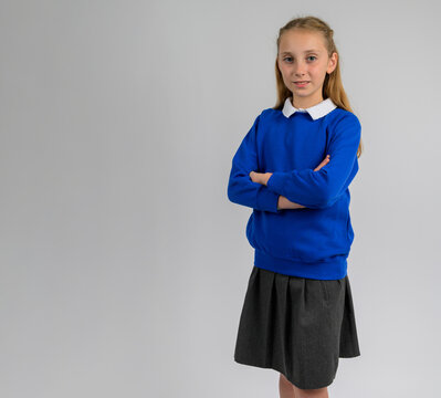 Confident schoolgirl standing with folded arms in blue pullover and grey skirt. Classic children’s school uniform showcasing cozy knit texture, smart classroom style, and autumn academic fashion