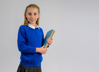 Smiling schoolgirl in blue pullover and grey skirt holding colorful folders. Classic British school uniform, children’s academic fashion and back-to-school education theme on neutral background