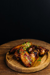 Delicious grilled chicken wings on wooden plate with herbs