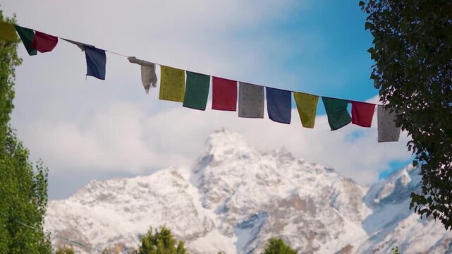 Closeup shot of colorful Buddhist Tibetan prayer flags in front of snowy Himalayan mountain peaks during the winter season as seen from Keylong in Lahaul and Spiti district, Himachal Pradesh, India.