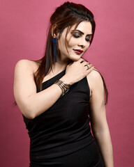 Confident and elegant woman posing gracefully in a one-shoulder black dress against a pink backdrop. Symbolizing fashion, beauty, and sophistication.