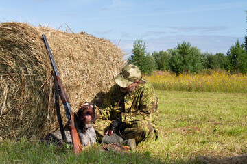 A hunter strokes a dog near a hay bale