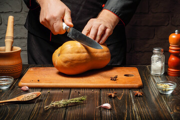 A chef in a rustic kitchen is slicing a squash on a wooden cutting board. Various spices and kitchen tools are arranged around, adding to the cooking ambiance