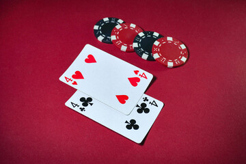 Two playing cards depicting four hearts and four clubs lie next to several poker chips on a red table. This scene captures a moment of card play