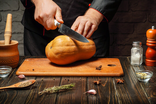 A chef in a rustic kitchen is slicing a squash on a wooden cutting board. Various spices and kitchen tools are arranged around, adding to the cooking ambiance