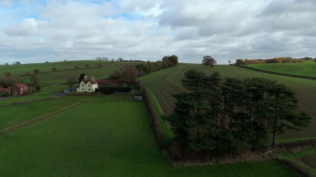 Aerial view of a quaint house nestled amongst rolling green fields, with contrasting textures of trees and cloudy skies, Nottingham, England, United Kingdom.